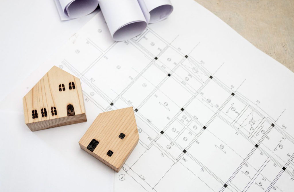 Imagem ilustrativa para investir em imóveis com casa em miniatura e planta ao fundo.