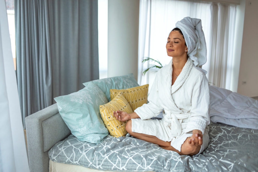 Mulher meditando em um quarto bem decorado, com cores calmas. Imagem ilustrativa para texto O que é cromoterapia.