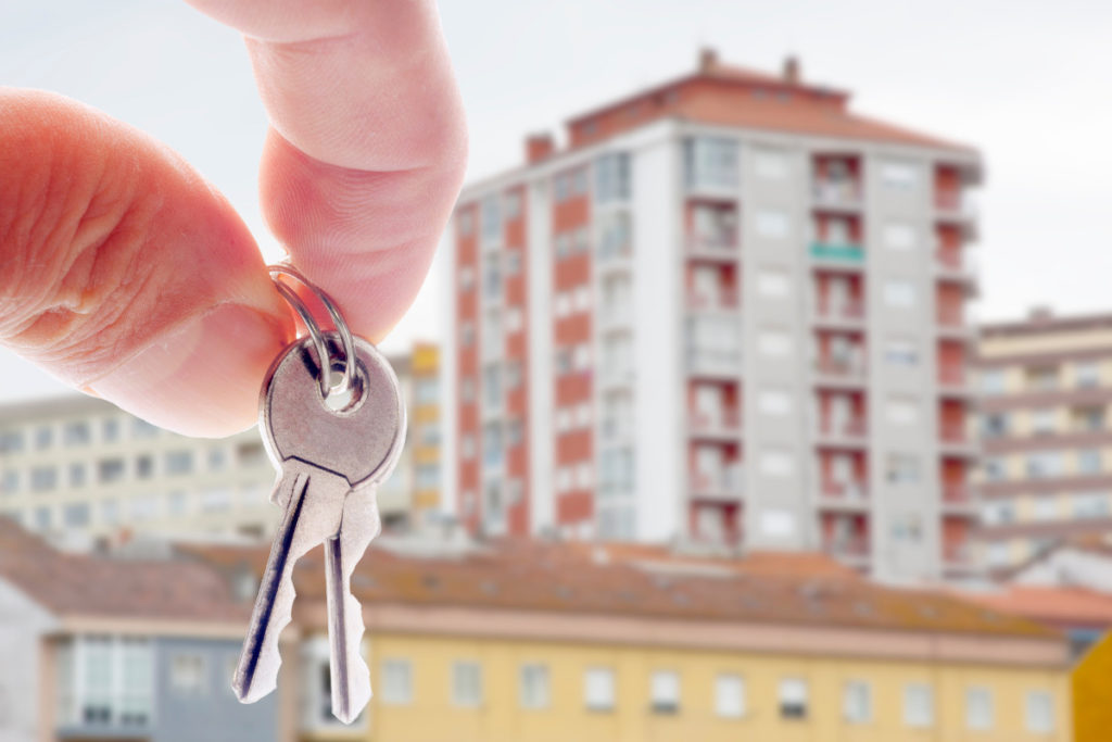Pessoa segurando chave de imóvel com apartamentos ao fundo. Imagem ilustrativa para texto o que é ipca.