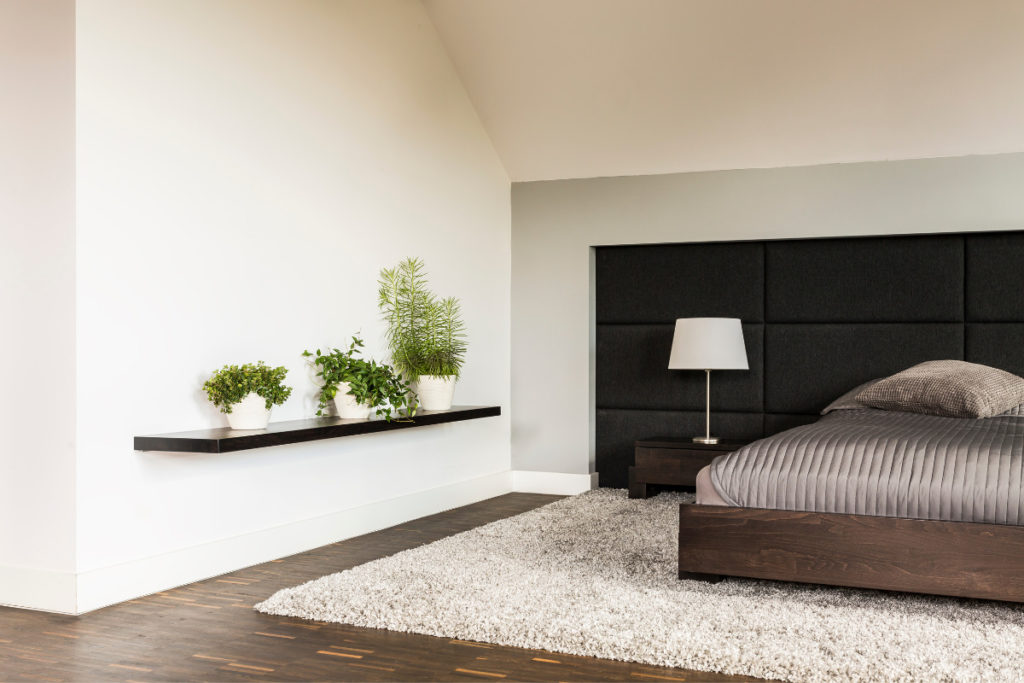 decoração neutra para quarto minimalista com cama e cabeceira preta, tapete e algumas plantas.
