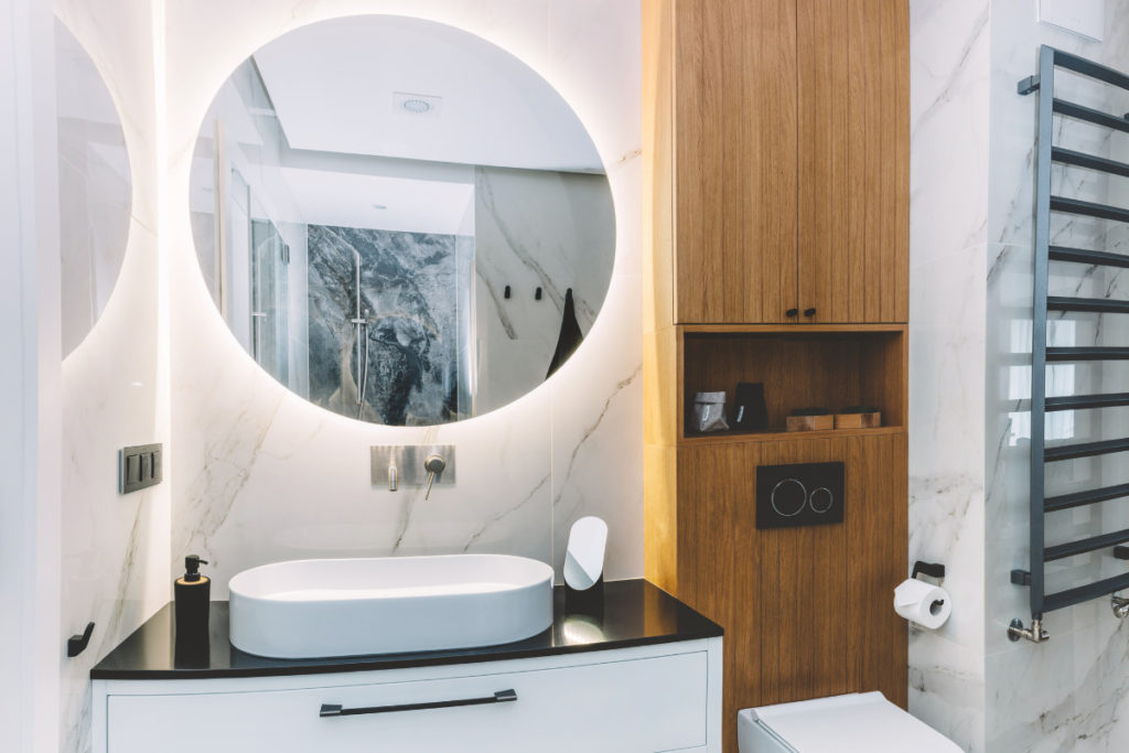 banheiro decorado com mármore, madeira e espelho grande com luzes. Imagem ilustrativa para texto banheiros modernos.