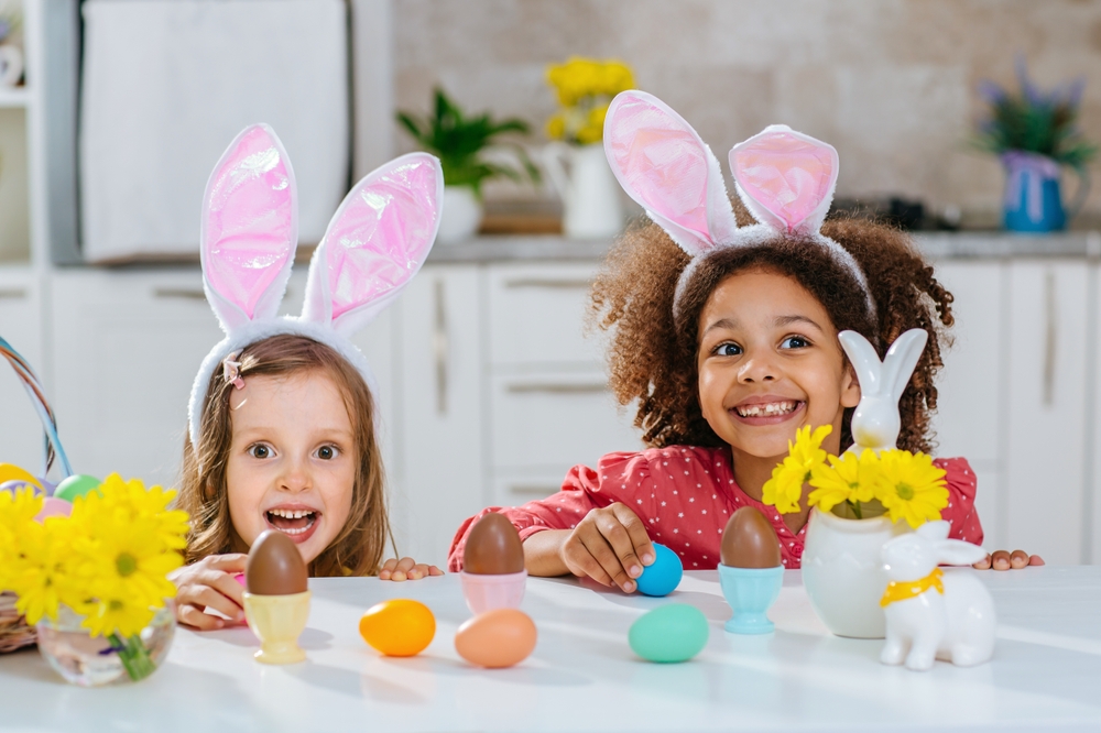 Duas meninas brincando com orelhinhas de coelho e vários ovos de Páscoa