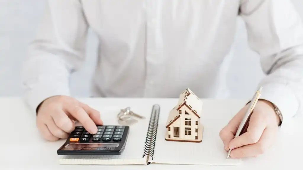 Valorização de imóveis: guia para identificar boas oportunidades Cálculo de valorização de imóveis com calculadora, caderno e maquete de casa sobre mesa, representando planejamento financeiro