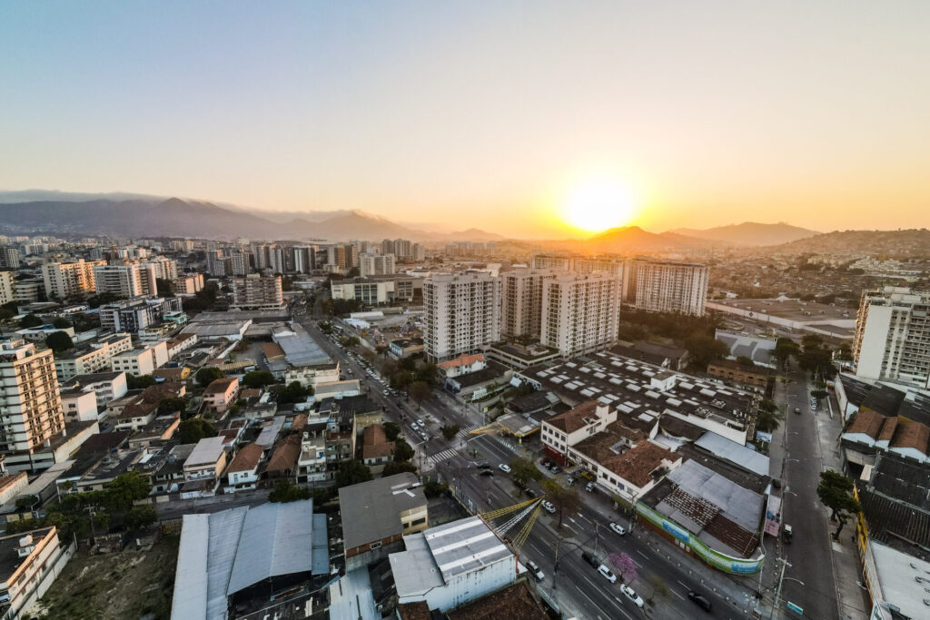 Zona Norte do Rio de Janeiro: conheça a região, vantagens e como é morar na área Imágem aérea da Avenida Dom Hélder Câmara com residências, industria e comércio com por do sol ao fundo na zona norte da cidade do Rio de Janeiro.